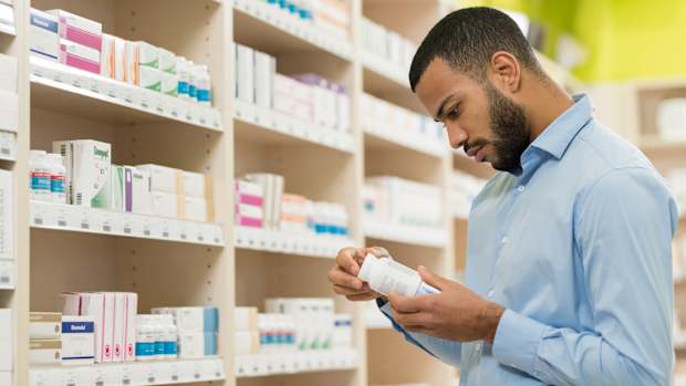 A man in a blue shirt holding a bottle of probiotic supplements as he stands in front of a shelf full of similar products